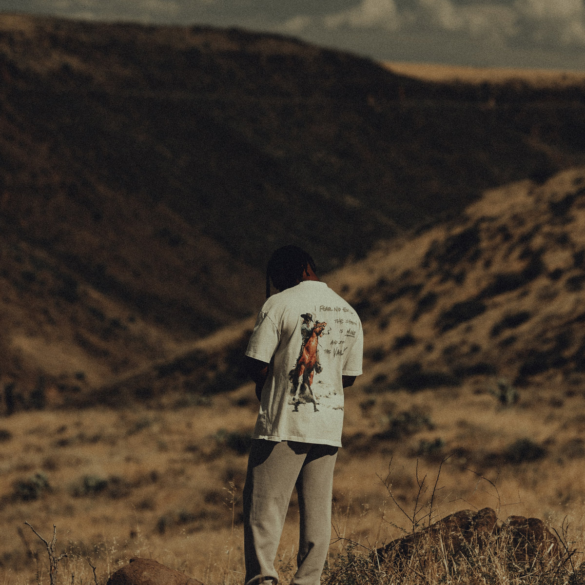 An athlete in the cream Iron Outlaw tee and cinder waffle sweatpants on a canyon ridge