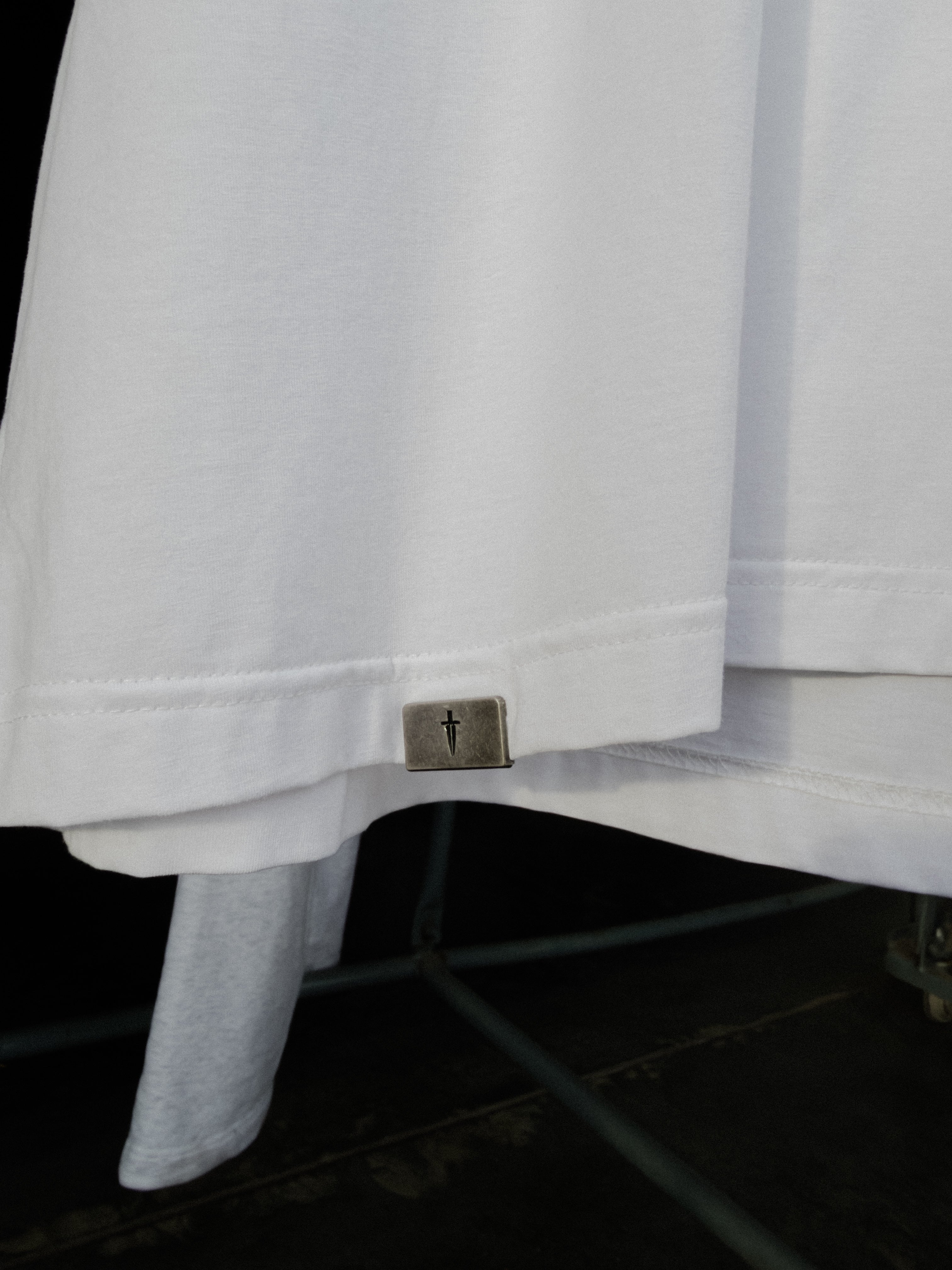 Signature metal tab at the bottom hem of the white tee