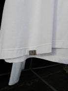 Signature metal tab at the bottom hem of the white tee