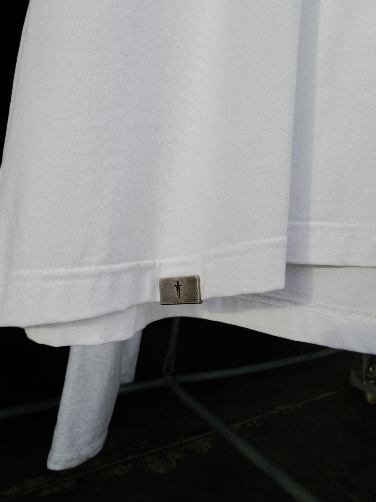 Signature metal tab at the bottom hem of the white tee